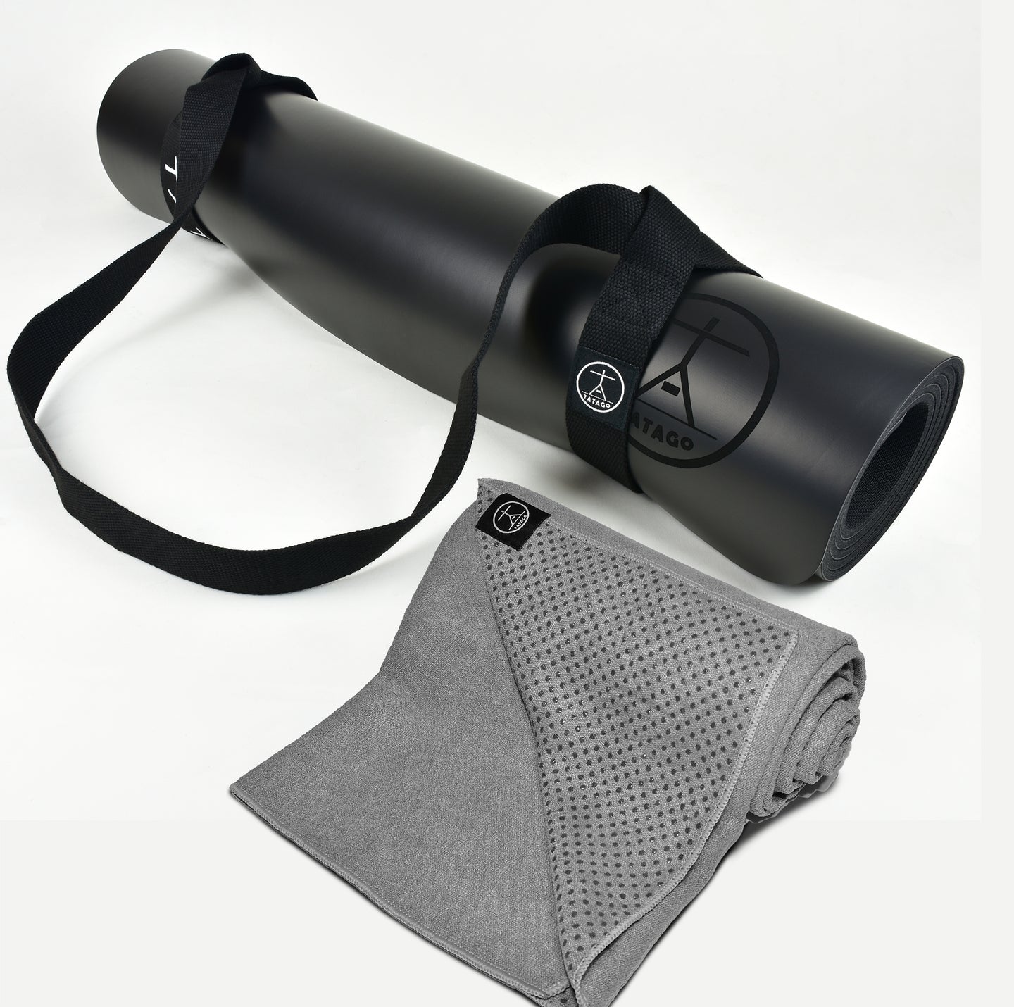 Black rubber yoga mat with strap and gray yoga towel on a white background