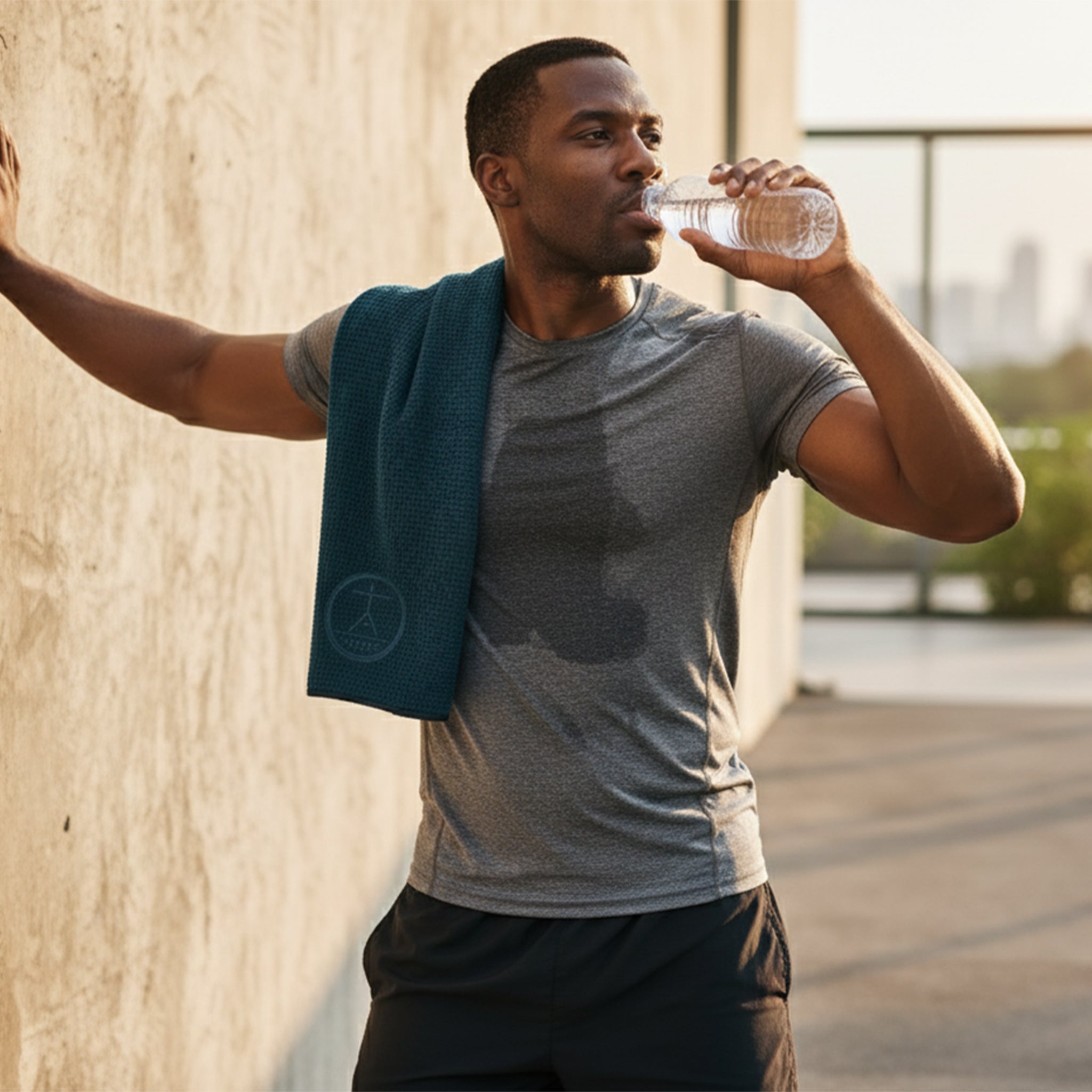 A man with a sweat rag on his shoulder, drinking water after a workout or run.