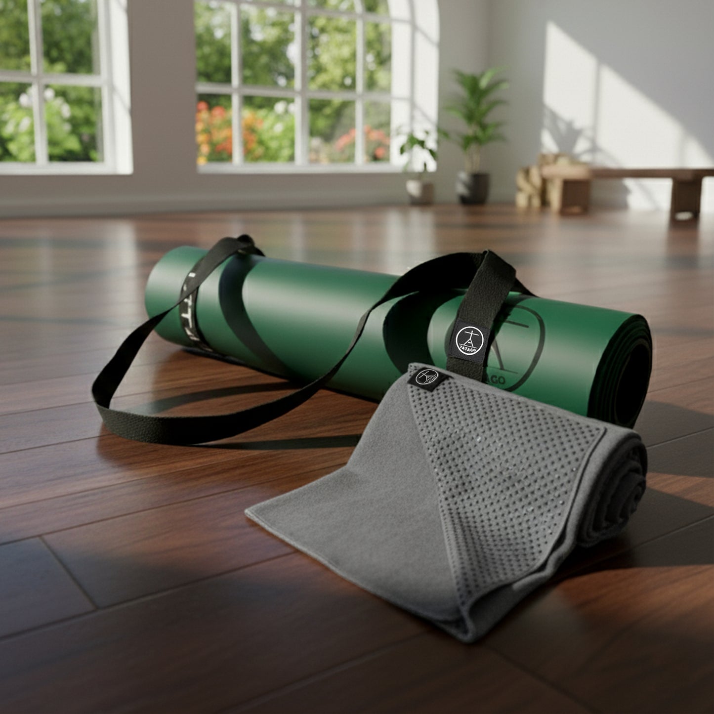 Extra large green natural rubber yoga mat with XL gray silicone grip yoga towel and carry strap laying in a bright yoga studio for hot yoga Pilates and sweaty practice